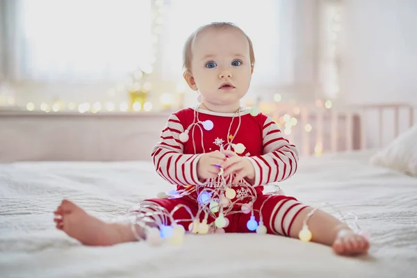 Lycklig liten baby flicka klädd i pyjamas leker med nyår träddekorationer — Stockfoto