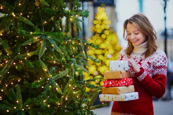Happy young girl in holiday sweater with pile of Christmas presents — Stock Photo, Image