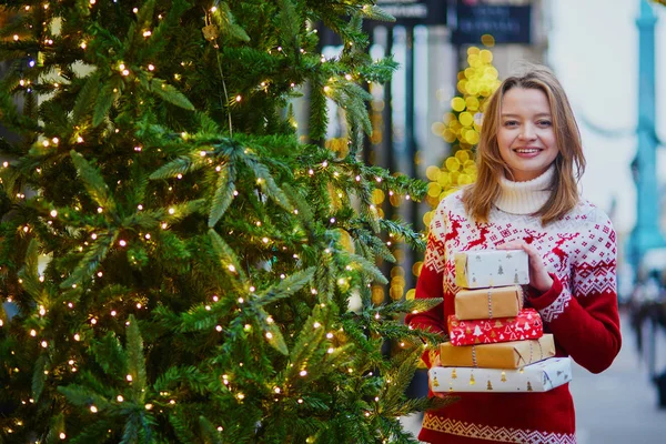 Happy young girl in holiday sweater with pile of Christmas presents — Stock Photo, Image