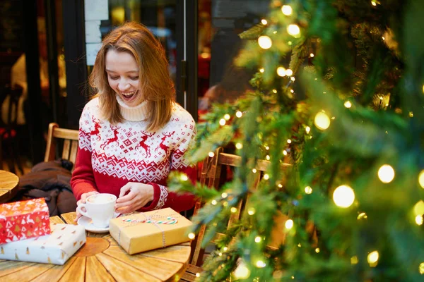 Девушка в праздничном свитере пьет кофе или горячий шоколад в кафе, украшенном на Рождество — стоковое фото