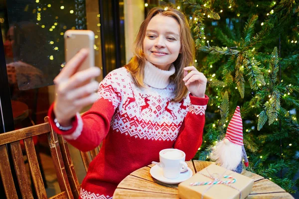 Jovencita alegre en suéter de vacaciones en la cafetería decorada para Navidad —  Fotos de Stock