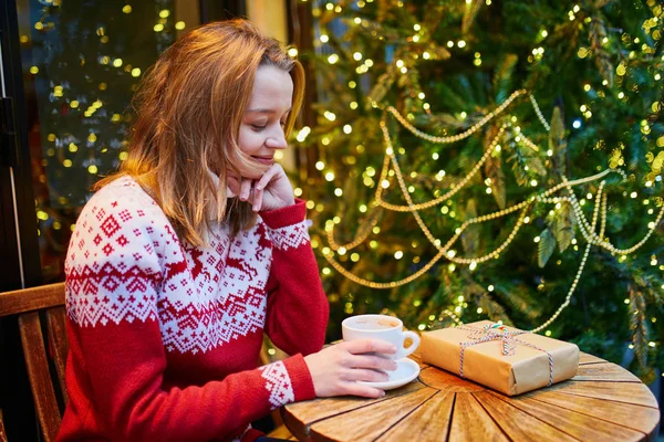 Girl in holiday sweater drinking coffee or hot chocolate in cafe decorated for Christmas — Stock Photo, Image