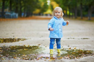 Sarı çizme giyen ve su birikintisinde zıplayan çocuk.