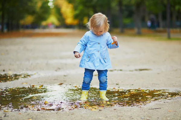 Niño con botas de lluvia amarillas y saltando en charco —  Fotos de Stock