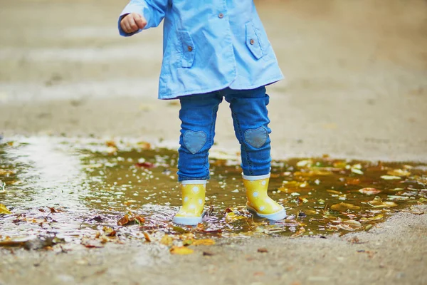 Niño con botas de lluvia amarillas y saltando en charco —  Fotos de Stock