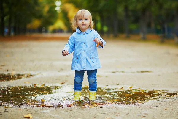 Criança usando botas de chuva amarelas e pulando na poça — Fotografia de Stock