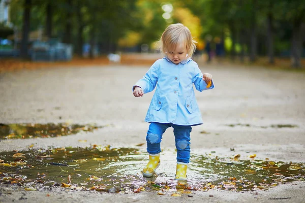 Kind draagt gele regenlaarzen en springt in plas — Stockfoto