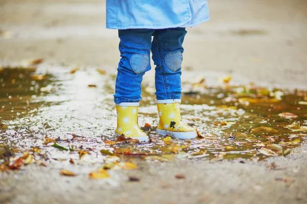 Criança usando botas de chuva amarelas e pulando na poça — Fotografia de Stock