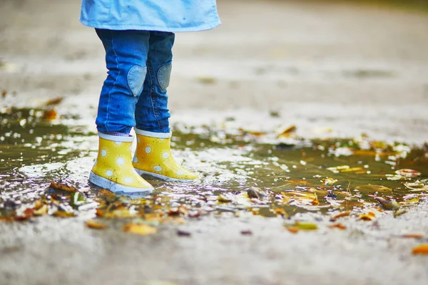 Дитина носить жовті дощові черевики і стрибає в калюжу — стокове фото