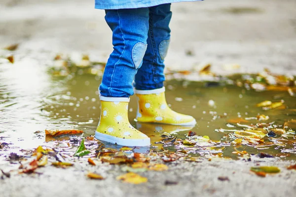 Criança usando botas de chuva amarelas e pulando na poça — Fotografia de Stock