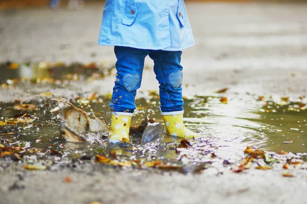 Kind draagt gele regenlaarzen en springt in plas — Stockfoto