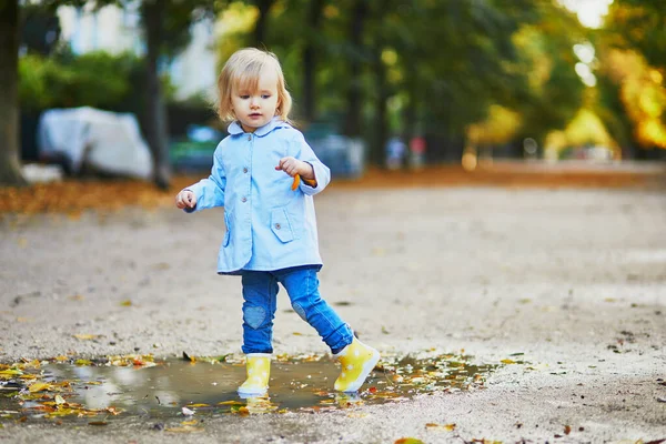 Criança usando botas de chuva amarelas e pulando na poça — Fotografia de Stock