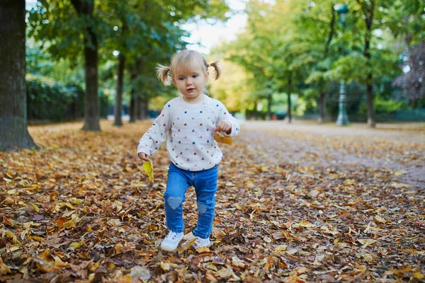 Rozkošné veselé batole dívka shromažďuje žluté podzimní listí v parku — Stock fotografie