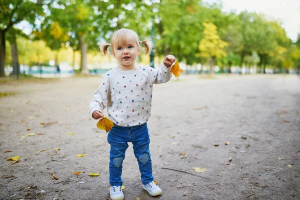 Rozkošné veselé batole dívka shromažďuje žluté podzimní listí v parku — Stock fotografie