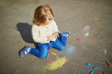 Asfalta renkli tebeşirler çizen sevimli küçük kız. Küçük çocuklar için açık hava aktiviteleri ve yaratıcı oyunlar