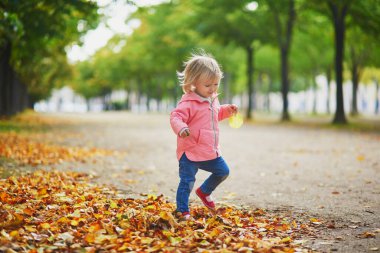 Paris, Fransa 'daki Tuileries bahçesinde koşan sevimli neşeli küçük kız. Mutlu çocuk sıcak ve güneşli sonbahar gününün tadını çıkarıyor. Çocuklar için açık hava sonbahar aktiviteleri