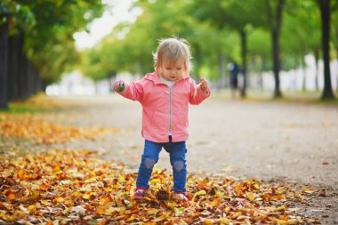 Paris, Fransa 'daki Tuileries bahçesinde koşan sevimli neşeli küçük kız. Mutlu çocuk sıcak ve güneşli sonbahar gününün tadını çıkarıyor. Çocuklar için açık hava sonbahar aktiviteleri