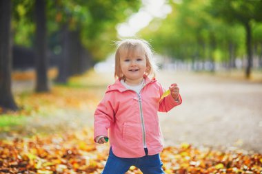 Paris, Fransa 'daki Tuileries bahçesinde koşan sevimli neşeli küçük kız. Mutlu çocuk sıcak ve güneşli sonbahar gününün tadını çıkarıyor. Çocuklar için açık hava sonbahar aktiviteleri