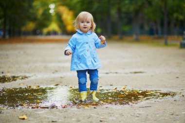 Sarı çizme giyen ve sonbahar günü su birikintisine atlayan bir çocuk. Tatlı küçük kız yağmurlu bir günde parkta su ve çamurla eğleniyor. Çocuklar için açık hava sonbahar aktiviteleri