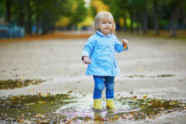 Sarı çizme giyen ve sonbahar günü su birikintisine atlayan bir çocuk. Tatlı küçük kız yağmurlu bir günde parkta su ve çamurla eğleniyor. Çocuklar için açık hava sonbahar aktiviteleri