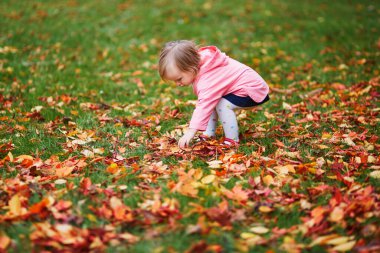 Fransa 'nın Paris kentindeki Tuileries bahçesinde sonbahar yapraklarını toplayan sevimli neşeli küçük kız. Mutlu çocuk sıcak ve güneşli sonbahar gününün tadını çıkarıyor. Çocuklar için açık hava sonbahar aktiviteleri