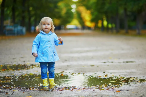 黄色のレインブーツを着て秋の日に水たまりに飛び込む子供 雨の日に公園で水と泥で楽しんでいる愛らしい幼児の女の子 子供のための屋外秋の活動 — ストック写真