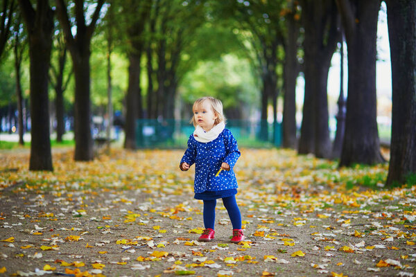 Adorable cheerful toddler girl running in autumn park in Paris, France. Happy child enjoying warm and sunny fall day. Outdoor autumn activities for kids