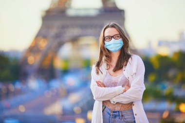 Paris 'teki Eyfel Kulesi' nin yanında duran ve Coronavirus salgını sırasında koruyucu maske takan genç bir kız. Fransa 'da salgın ve tecrit. Karantinadan sonra Fransa 'da tatil yapan turistler