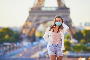 Paris 'teki Eyfel Kulesi' nin yanında duran ve Coronavirus salgını sırasında koruyucu maske takan genç bir kız. Fransa 'da salgın ve tecrit. Karantinadan sonra Fransa 'da tatil yapan turistler