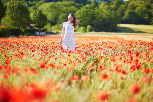 Beautiful young woman in white dress walking in poppy field on a summer day. Girl enjoying flowers in countryside