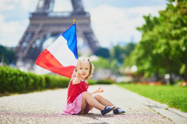 Beautiful toddler girl with French national tricolor flag near the Eiffel tower in Paris, France. 14 July (Bastille day), main French national holiday clipart