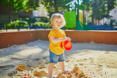 Sevimli küçük kız kum havuzunda oyun parkında eğleniyor. Bebek kum kalıplarıyla oynuyor ve çamur yapıyor. Çocuklar için açık hava yaratıcı aktiviteler