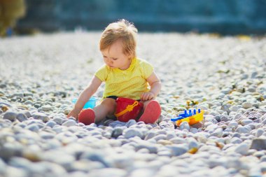 Sevimli küçük kız sahilde çakıl taşlarıyla oynuyor. Küçük çocuk Etretat, Normandiya, Fransa 'da deniz kenarında eğleniyor. Çocuklar için açık hava aktiviteleri