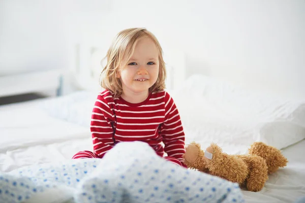 醒来后 穿着条纹红白相间的睡衣坐在床上 快乐地蹒跚学步的小女孩 幼儿日间小睡 — 图库照片