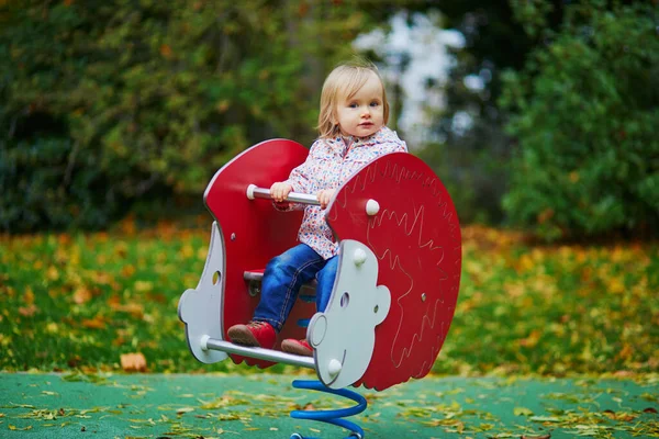 可爱的蹒跚学步的小女孩在秋天的操场上玩着春车 为儿童举办的户外秋季活动 — 图库照片