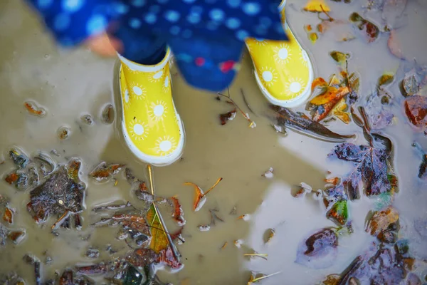 黄色のレインブーツを着て 秋の日に汚れた水たまりに飛び込む子供 幼児の女の子は雨の日に公園で水と泥で楽しんでいます 子供のための屋外秋の活動 — ストック写真