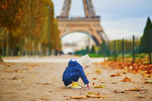 青いレインコートを着た愛らしい幼児の女の子は フランスのパリのエッフェル塔の近くに黄色の落ち葉を集めています 暖かく晴れた秋の日を楽しむ幸せな子供 — ストック写真