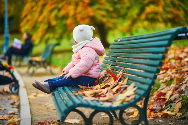 ベンチに座って フランスのパリの公園で落ち葉で遊んでいる愛らしい幼児の女の子 美しい秋の日を楽しむ幸せな子供 子供のための屋外秋の活動 — ストック写真