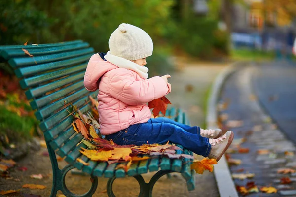 ベンチに座って フランスのパリの公園で落ち葉で遊んでいる愛らしい幼児の女の子 美しい秋の日を楽しむ幸せな子供 子供のための屋外秋の活動 — ストック写真