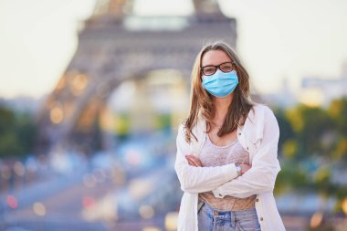 Paris 'teki Eyfel Kulesi' nin yanında duran ve Coronavirus salgını sırasında koruyucu maske takan genç bir kız. Fransa 'da salgın ve tecrit. Karantinadan sonra Fransa 'da tatil yapan turistler