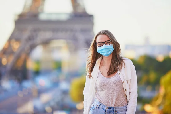 Young girl standing near the Eiffel tower in Paris and wearing protective face mask during coronavirus outbreak. Pandemic and lockdown in France. Tourist spending vacation in France after quarantine