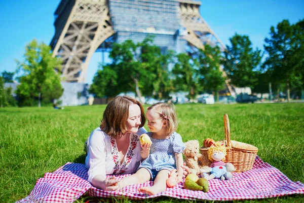 フランスのパリにあるエッフェル塔の近くでピクニックをしている若い女性 母と娘は夏の日に公園で一緒に楽しんでいます 屋外で健康的な軽食を楽しむ子供 — ストック写真