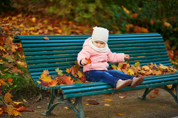 Urocza Dziewczynka Siedząca Ławce Bawiąca Się Spadającymi Liśćmi Parku Paryżu — Zdjęcie stockowe