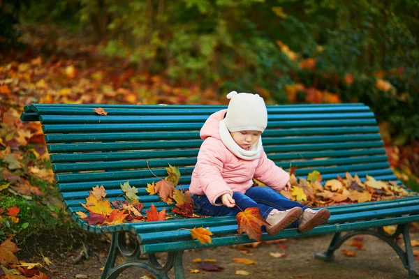 ベンチに座って フランスのパリの公園で落ち葉で遊んでいる愛らしい幼児の女の子 美しい秋の日を楽しむ幸せな子供 子供のための屋外秋の活動 — ストック写真