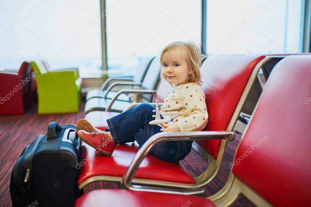 Adorable little toddler girl traveling by plane. Child sitting in gate and waiting for the flight. Traveling abroad with kids. Unaccompanied minor concept