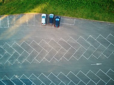 Açık hava parkı manzaralı ve üzerinde üç araba park edilmiş. İşaret çizgileri olan otopark