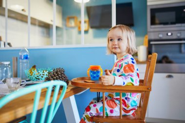 Evdeki mutfakta kahvaltı ederken yüksek sandalyede oturan pijamalı sevimli bir kız.