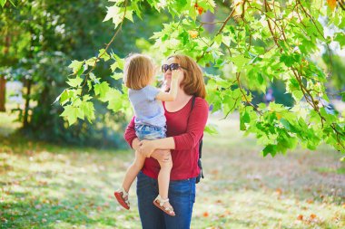 Küçük tatlı kızını kucağında tutan mutlu genç anne. Parkta güneşli bir günde kadın ve çocuk birlikte eğleniyor.