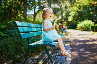 Sevimli küçük kız dışarıda bankta oturuyor ve güneşli bir yaz gününde atıştırıyor. Mutlu çocuk parkta yürüyor. Çocuklar için yürüyüş ve sağlıklı beslenme
