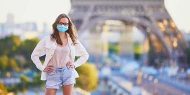 Paris 'te Eyfel kulesinin yanında duran ve koruyucu yüz maskesi takan bir kız. Salgın sırasında Fransa 'da turist tatili